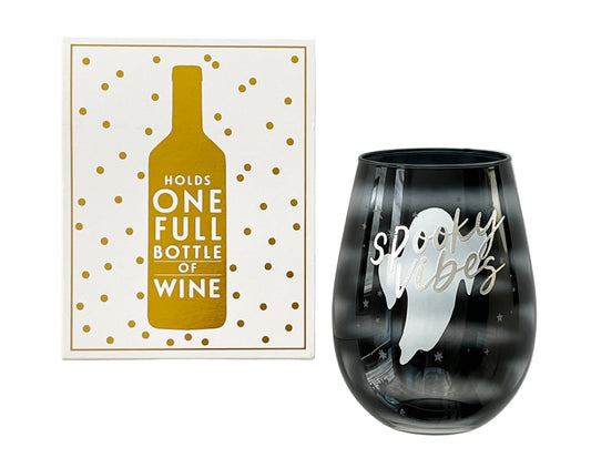 A black-to-clear gradient stemless wine glass with a white ghost and 'spooky vibes' script, shown next to its white and gold gift box featuring a wine bottle graphic and the text 'HOLDS ONE FULL BOTTLE OF WINE'.